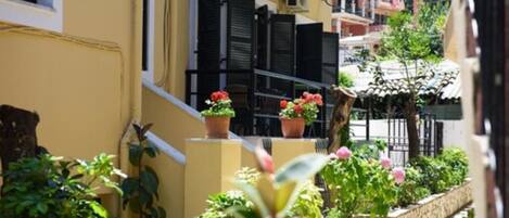 A narrow street with yellow buildings, black shutters, and potted plants.