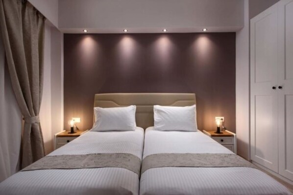 Una cama doble con cabecera color beige, dos mesitas de noche con lámparas y una pared de tonos neutros.