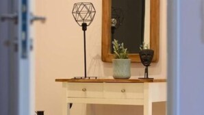 Una habitació amb un escriptori blanc, un tamboret de fusta, un mirall, una làmpada geomètrica i una petita planta.