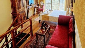 A spacious room with a large bed, a red sofa, a wooden staircase, and a view of the outdoors.