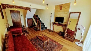 A living room with a red sofa, wooden flooring, a staircase, a fireplace, and a TV.