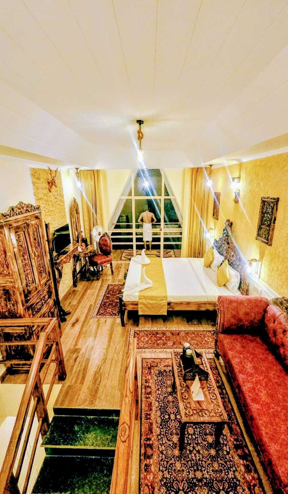 Camera d'albergo con un letto, un divano rosso, un armadio in legno, un tavolino e una scala che conduce a un balcone.