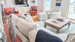 Un salon spacieux avec un plafond haut, un ventilateur de plafond, un grand téléviseur et une vue sur l’extérieur grâce à une grande fenêtre.