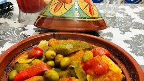 Ein traditionelles marokkanisches Tajine-Gericht mit Gemüse und Oliven, serviert auf einer gemusterten Tischdecke.