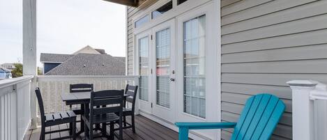 Una terraza techada al aire libre con una mesa y sillas, un sillón Adirondack azul y una puerta blanca con ventanas.