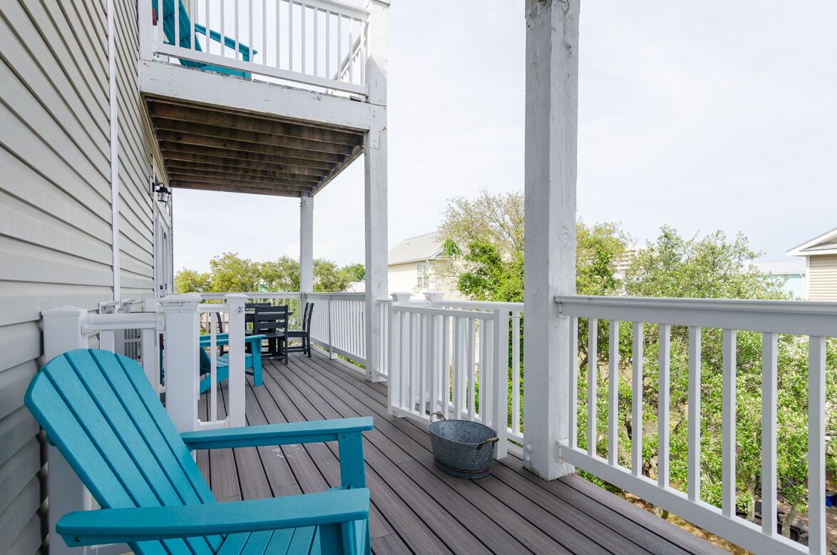 A wooden deck with white railings, a blue Adirondack chair, and a bucket.