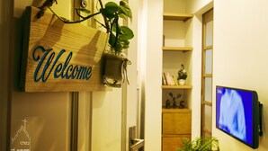 Un panneau d’accueil en bois, agrémenté d’une plante, avec une télévision et une étagère contenant des livres et des objets décoratifs en arrière-plan.
