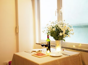 A table set with a bottle of wine, glasses, a plate of food, and a vase of flowers by a window overlooking the sea. - 40 sqm deluxe one-bedroom apartment#302_close to old quarter (Dong Da)