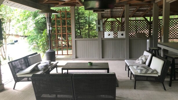 Eine Terrasse im Freien mit Korbmöbeln, einem Flachbildfernseher und einem Holzzaun.
