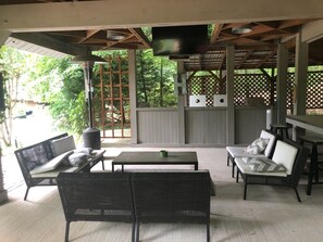 Eine Terrasse im Freien mit Korbmöbeln, einem Flachbildfernseher und einem Holzzaun.