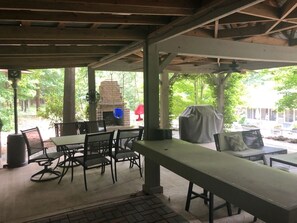 Eine überdachte Terrasse im Freien mit Tischen, Stühlen, einem Kamin aus Ziegeln und einem überdachten Grillbereich.