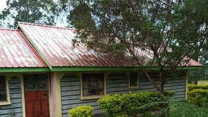 A small, single-story building with a red roof and green trim. It has a red door and windows with wooden frames. The building is surrounded by a well-maintained lawn and a few small trees. - Property is located at kanusin village near Chepeyan pry school,near main roads (Bomet)