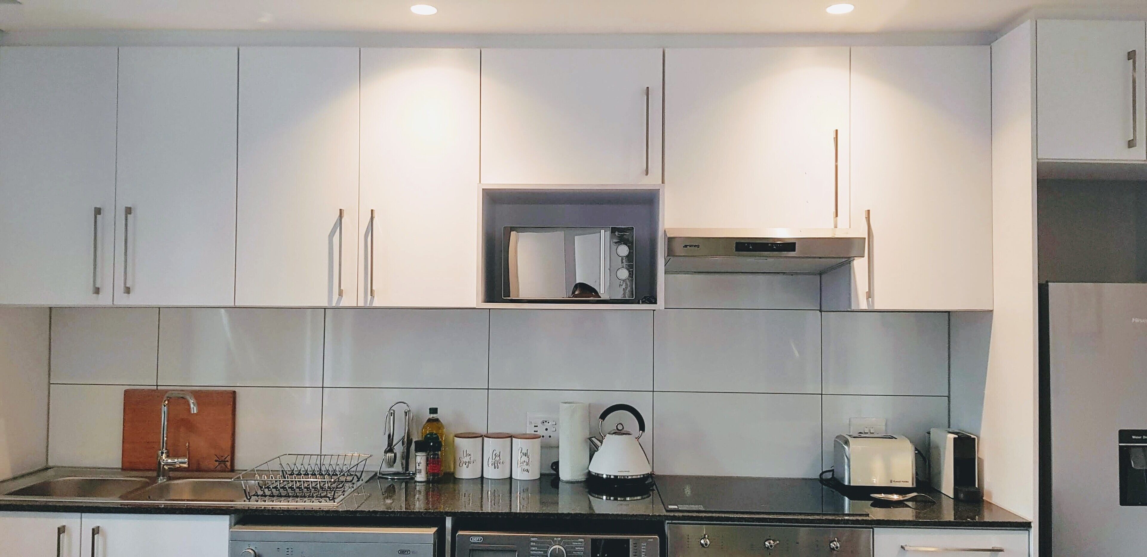 A modern kitchen with white cabinets, a stainless steel sink, and a built-in oven.