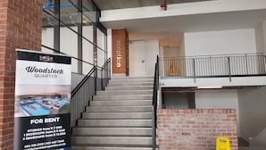 Eine Treppe führt zu einem Empfangsbereich mit einem Schild für 'Woodstock Quarter' und einer Vermietungsanzeige.