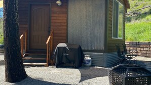 A small cabin with a wooden door, a covered grill, and a chair outside. - Eagle's Nest For Great Hikes, Local Breweries and Coffee Shops. (Lolo)
