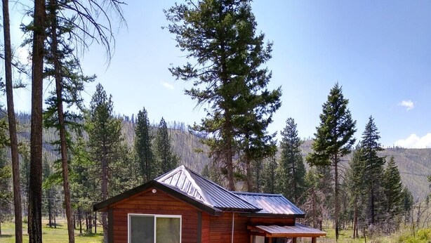 A wooden cabin with a metal roof, surrounded by a grassy area and trees. - Eagle's Nest For Great Hikes, Local Breweries and Coffee Shops. (Lolo)