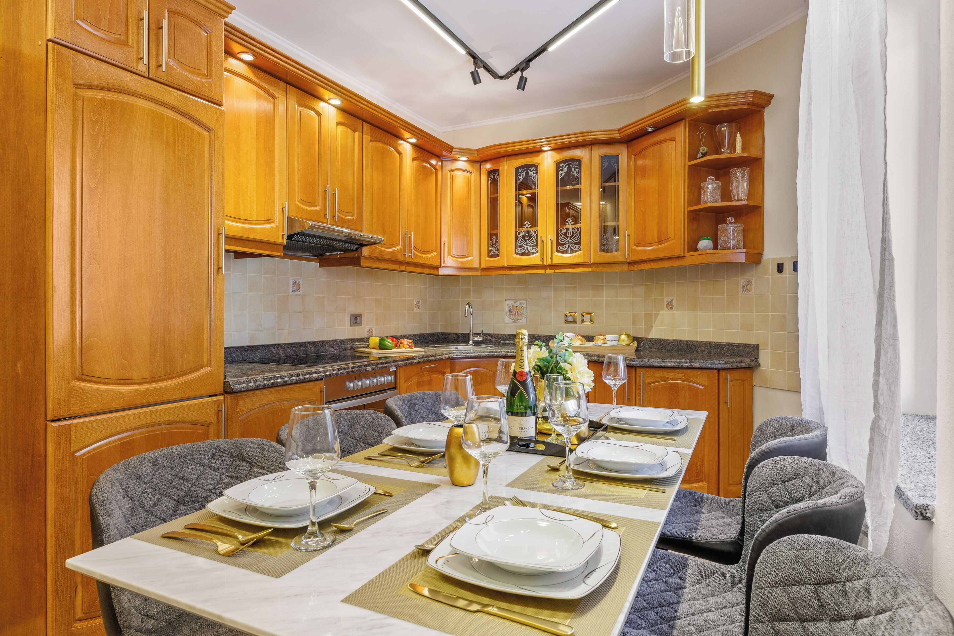 A modern kitchen with wooden cabinets, a marble countertop, and a dining area set for a meal.
