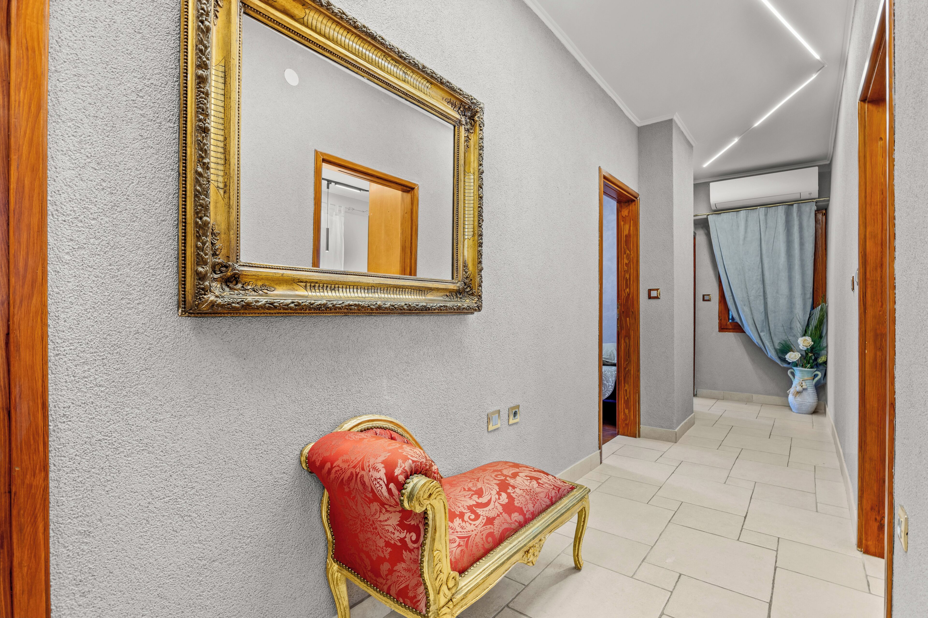 Un corridoio con una panca imbottita rossa, un ampio specchio decorato e una porta che dà su un'altra stanza.