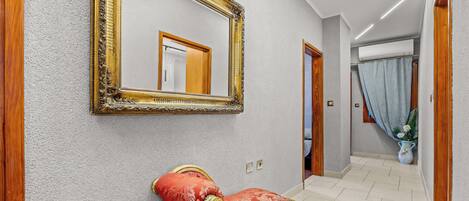 Un corridoio con una panca imbottita rossa, un ampio specchio decorato e una porta che dà su un'altra stanza.