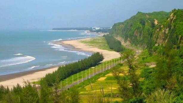 A coastal landscape with a beach, a road with guardrails, and a hilly terrain with vegetation. - Hotel Diamond Palace (Cox's Bazar)