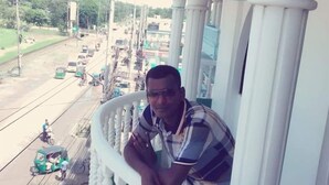 A man on a balcony with white balustrades overlooking a busy street with vehicles. - Hotel Diamond Palace (Cox's Bazar)