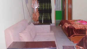 A small, compact room with a sofa, a bed, a wooden table, and a curtain. - Hotel Diamond Palace (Cox's Bazar)