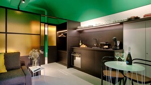 A compact living space with a sofa, a small table with a vase, a kitchenette, and a dining area with chairs.
