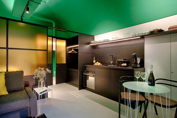 A compact living space with a sofa, a small table with a vase, a kitchenette, and a dining area with chairs. - Casa pacifico Napoli (Naples)