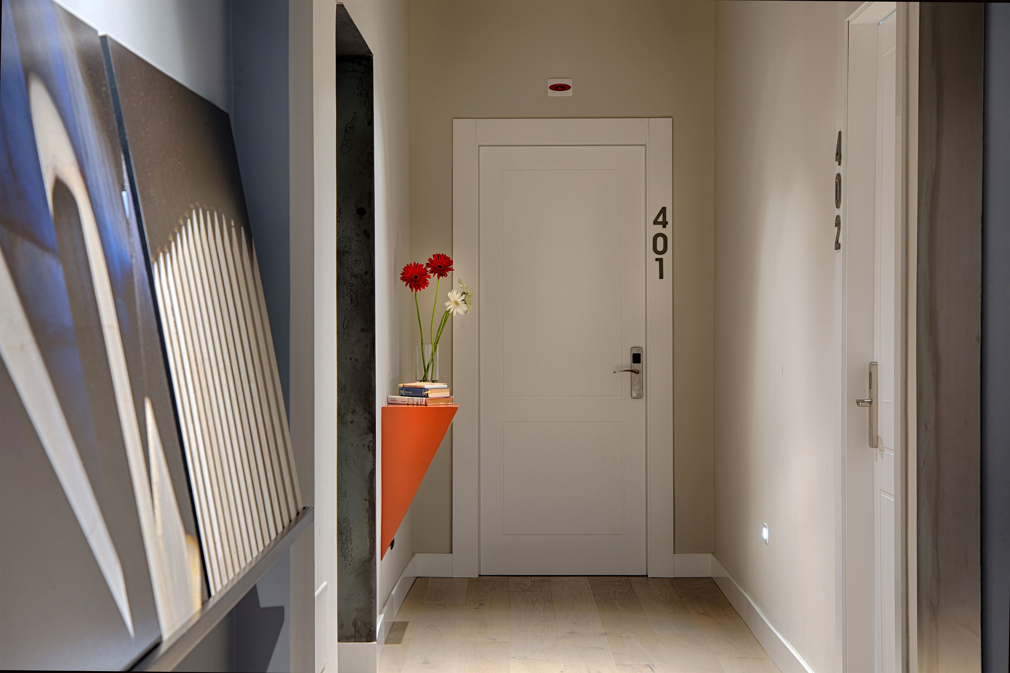 A hallway with a white door labeled "401", a small orange table with a vase of flowers, and a framed picture leaning against the wall.