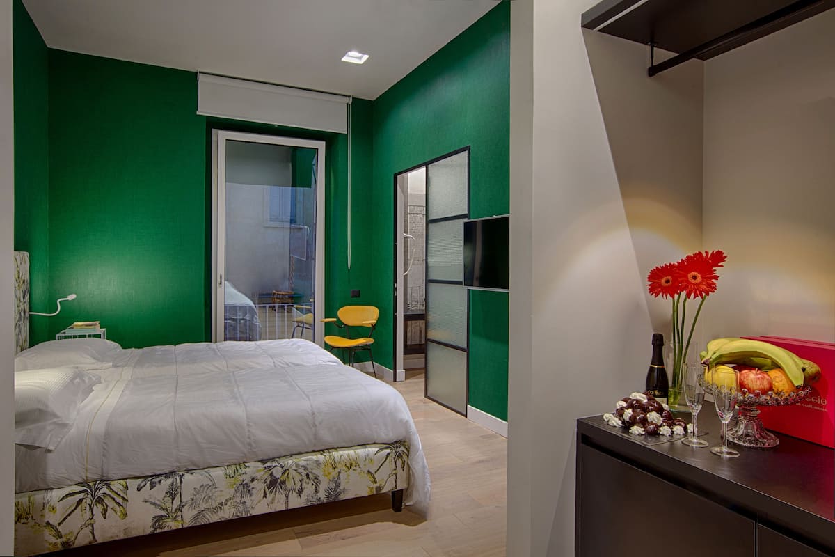 A bedroom with a bed, a desk with a vase of flowers, and a red chair.