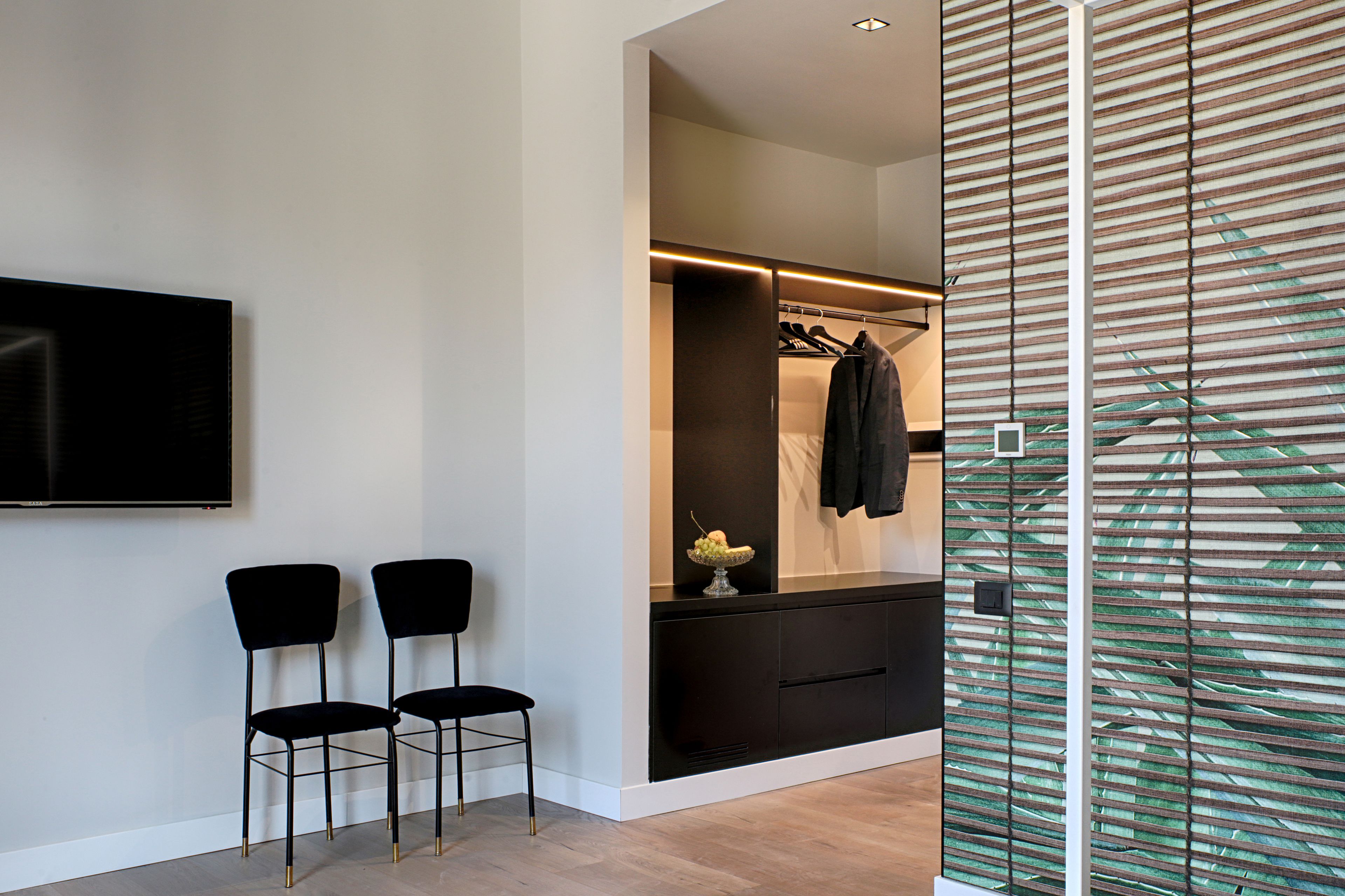 A modern room with a black sofa, two black chairs, a TV, a closet, and a decorative glass panel.