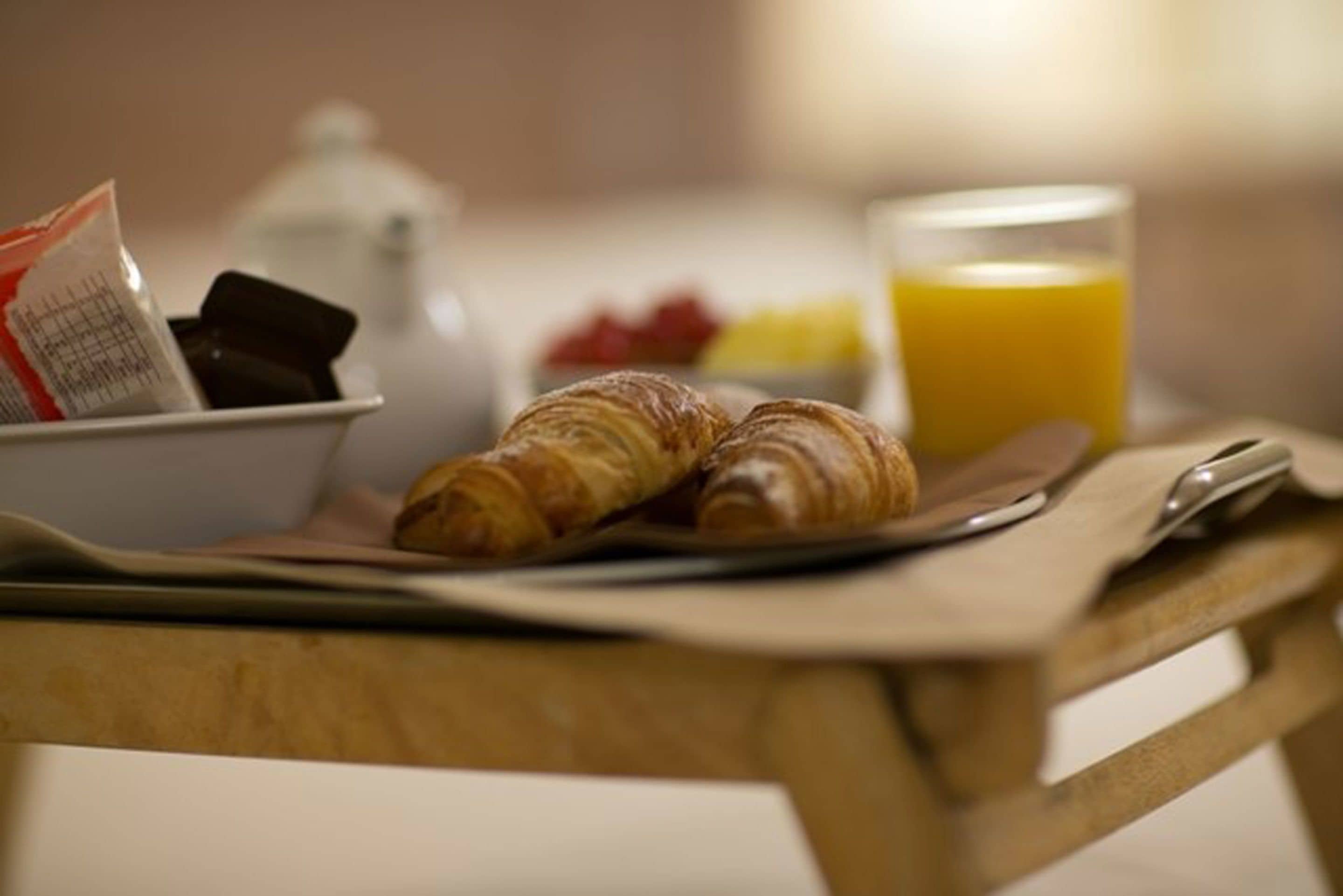 A breakfast setting with croissants, a glass of orange juice, and a bowl of fruit on a wooden table.