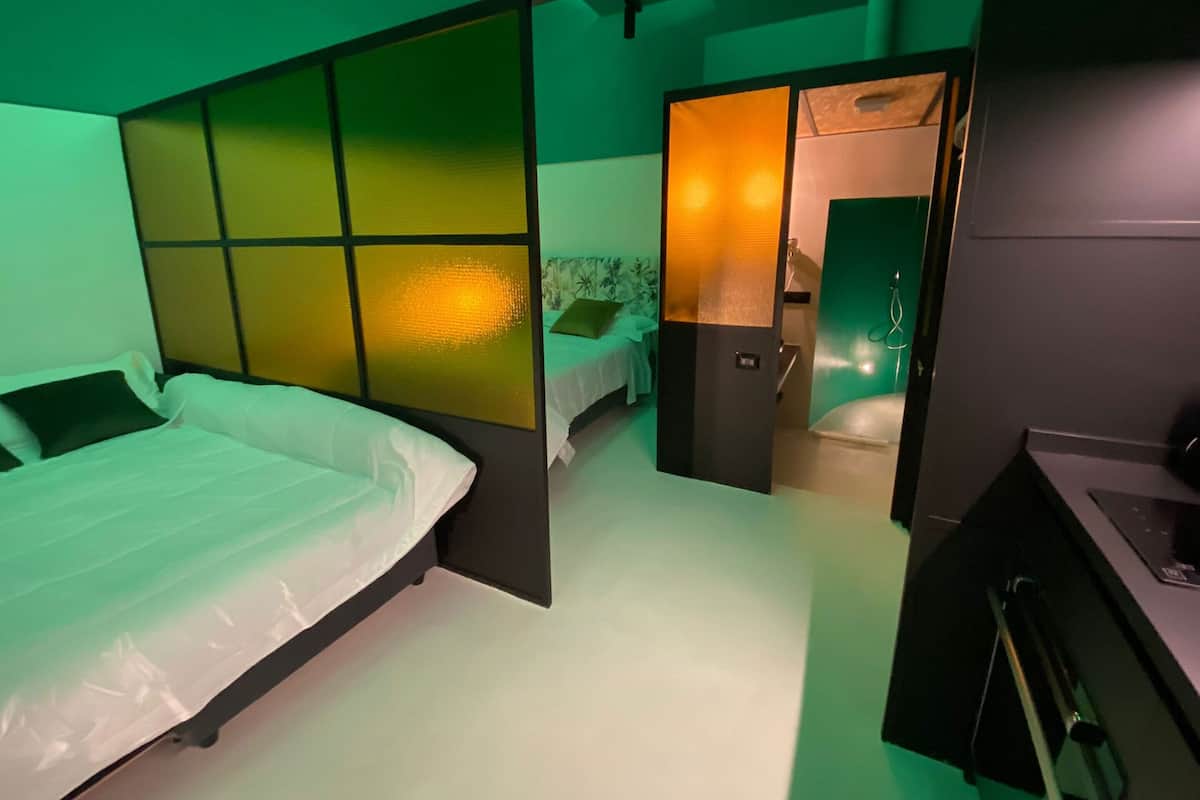 A modern hotel room with a bed, a small desk, and a bathroom visible through an open door.