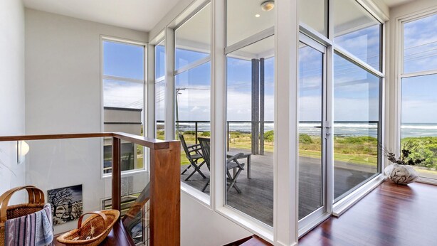 A spacious room with large windows offering ocean views, a wooden staircase, and a view of the deck with outdoor furniture. - Magnificent views over the Southern Ocean (PORT FAIRY)