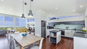 A modern kitchen with a view of the ocean, featuring a dining area with a wooden table and chairs, and a built-in bookshelf. - Magnificent views over the Southern Ocean (PORT FAIRY)
