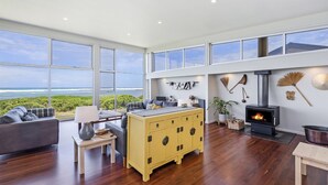 A spacious living room with a large window overlooking the ocean, a yellow cabinet, a fireplace, and a cozy seating area. - Magnificent views over the Southern Ocean (PORT FAIRY)