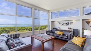 A spacious living room with large windows offering ocean views, a leather sofa, a wooden coffee table, and a minimalist decor style. - Magnificent views over the Southern Ocean (PORT FAIRY)
