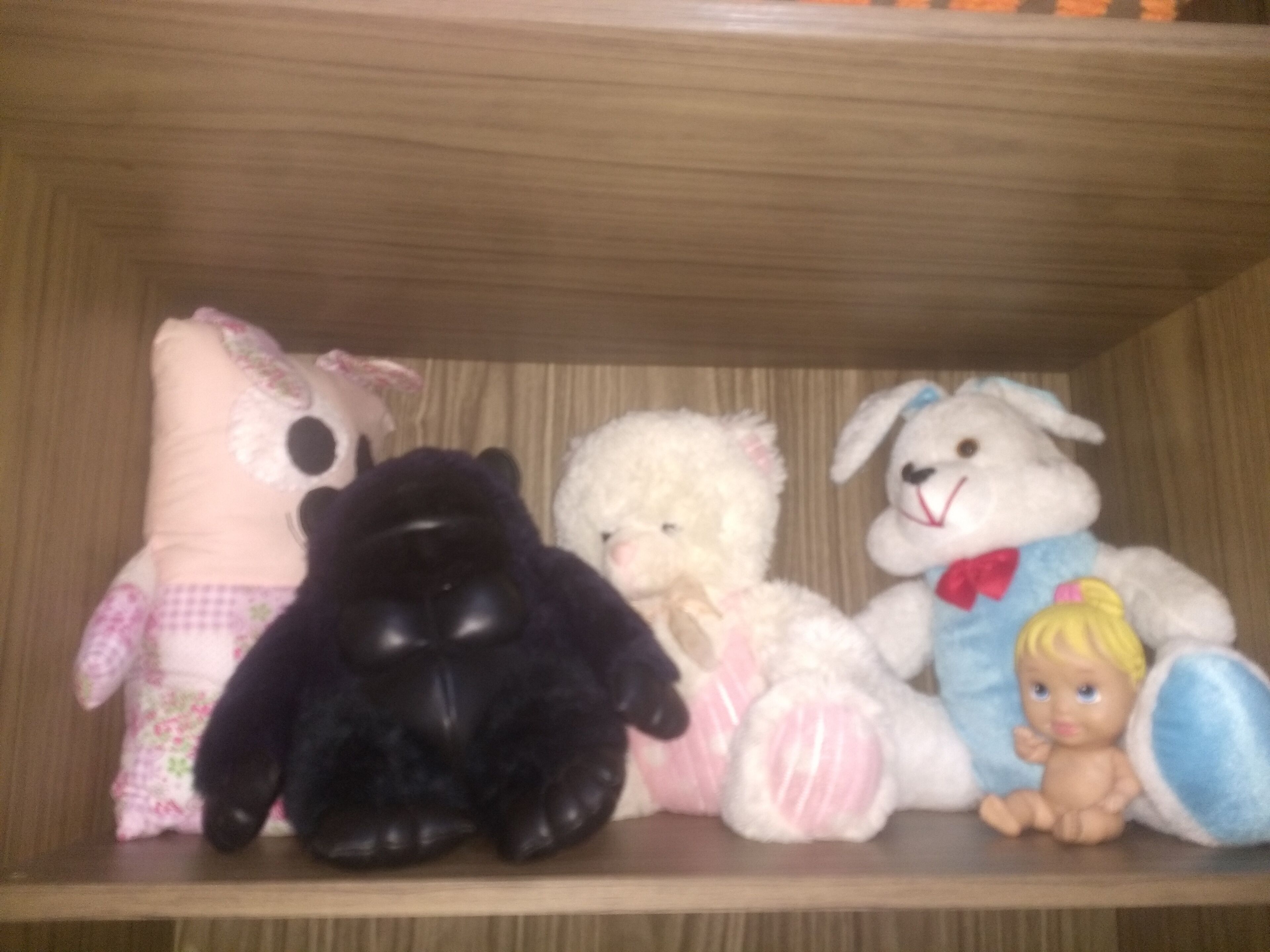 Hyllyllä on useita pehmoleluja, kuten musta gorilla, valkoinen karhu ja valkoinen pupu.