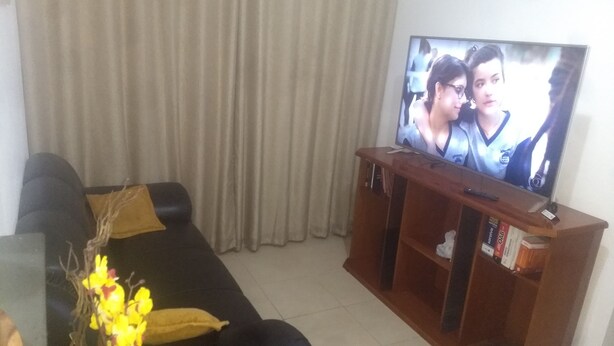 Un salón con un sofá negro, un mueble de entretenimiento de madera y un televisor que muestra una escena.