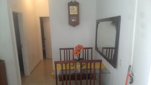 Un comedor con una mesa y sillas de madera, un jarrón con flores, un reloj de pared y un espejo.