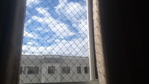 Una ventana con una cerca de malla metálica, vista de un edificio con varias ventanas y un cielo parcialmente nublado.