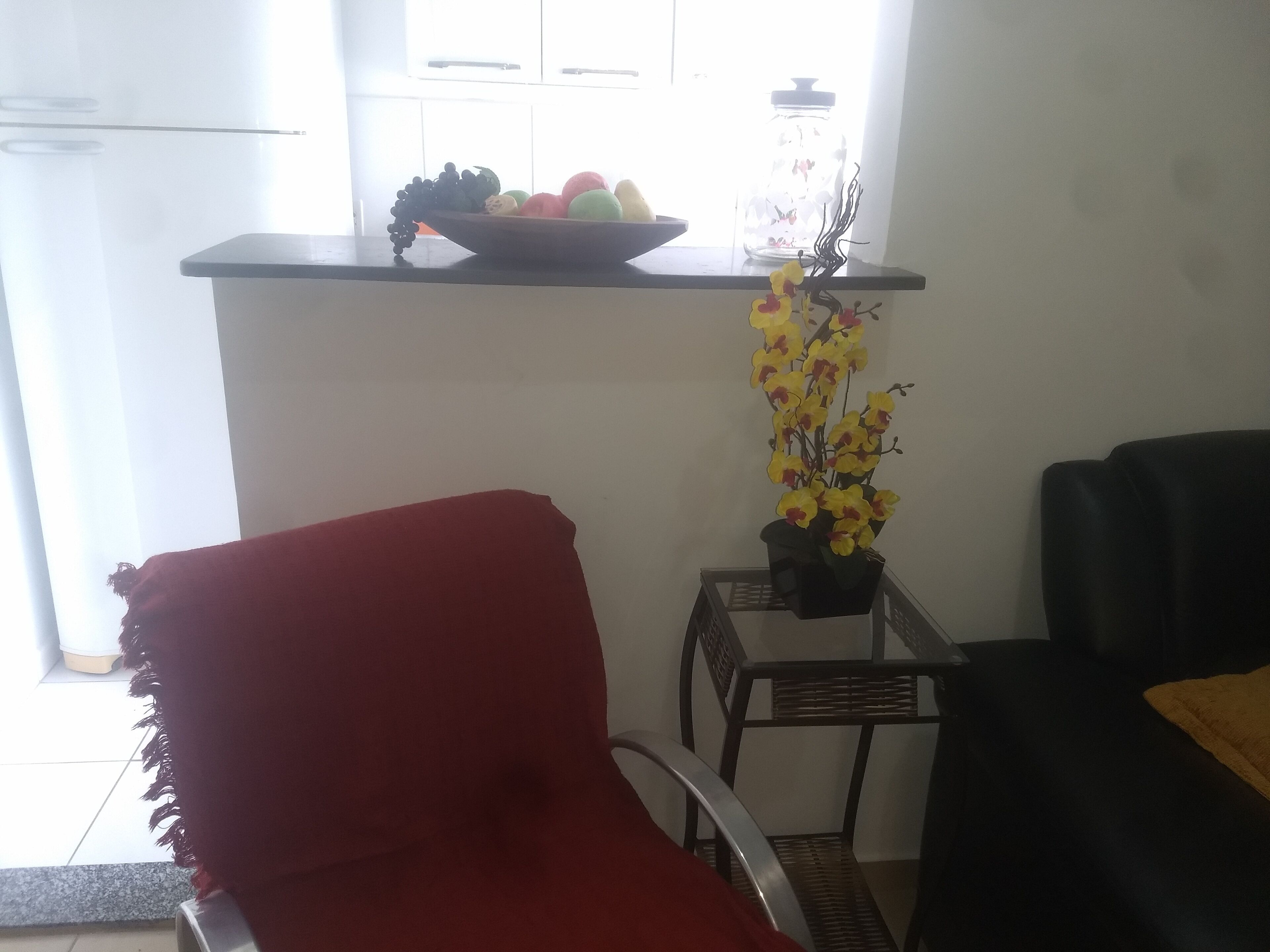 Un coin cuisine avec un panier de fruits posé sur une étagère, une orchidée en pot et une chaise rouge.