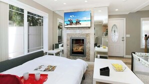 Ett hotellrum med en säng, en tv som är monterad ovanför en öppen spis, en matplats och en dörr som leder till ett annat rum.