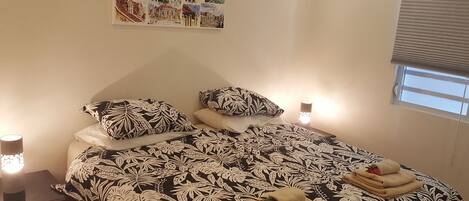A neatly made bed with a black and white leaf-patterned bedspread, two matching pillows, and a bedside table with a lamp.