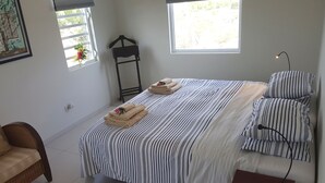 A bedroom with a bed, striped bedding, a chair, a nightstand, and a window with a view. - LUXURY HILLTOP VILLA "Het Catshuis" - Private Pool & Panoramic Views (Willemstad)