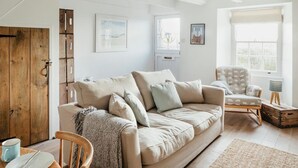 A cozy living room with a beige sofa, a wooden door, and a window with a view. - 17 Farmers Meadow (Penzance)