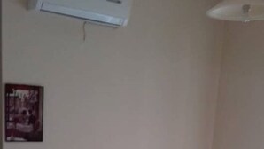 Ein Zimmer mit zwei Einzelbetten, weißer Bettwäsche, einem Holz-Kopfteil, einem Nachttisch, einer wandmontierten Klimaanlage und einem kleinen Bilderrahmen.