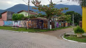 A paved street with a sidewalk, a bench, and a mural on a wall. - Maresias. Spacious and comfortable house. With 4 bedrooms and close to everything. (Sâo Sebastião)