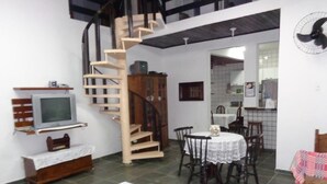 A compact living space with a spiral staircase, a dining area with a table and chairs, a television, and a small kitchen area. - Maresias. Spacious and comfortable house. With 4 bedrooms and close to everything. (Sâo Sebastião)