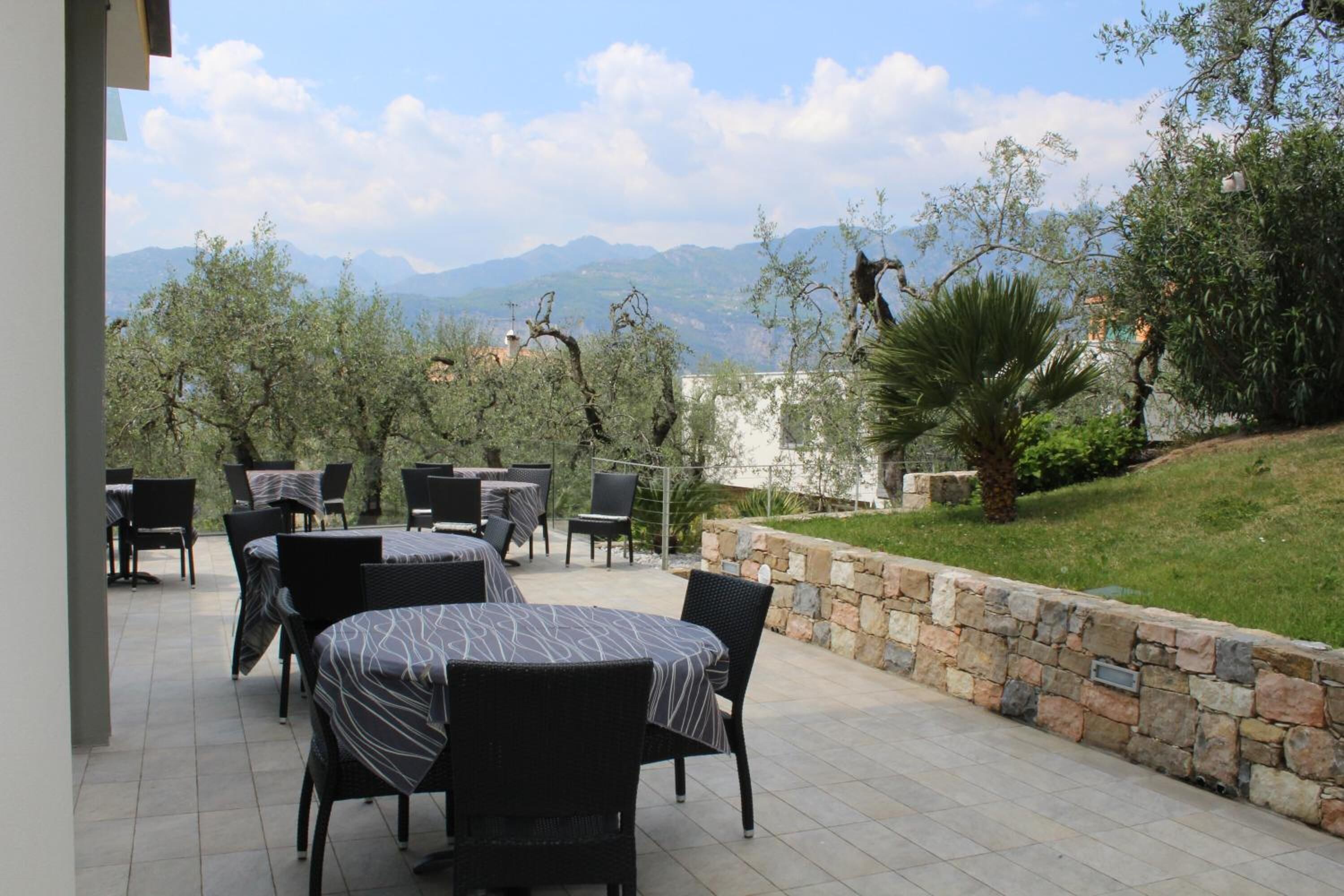 Un patio al aire libre con mesas y sillas, un muro de piedra y vistas a las montañas.
